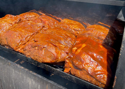 Smoked brisket cooking inside an open black smoker box with visible smoke, photographed in a real outdoor setting at The Berry Farm.