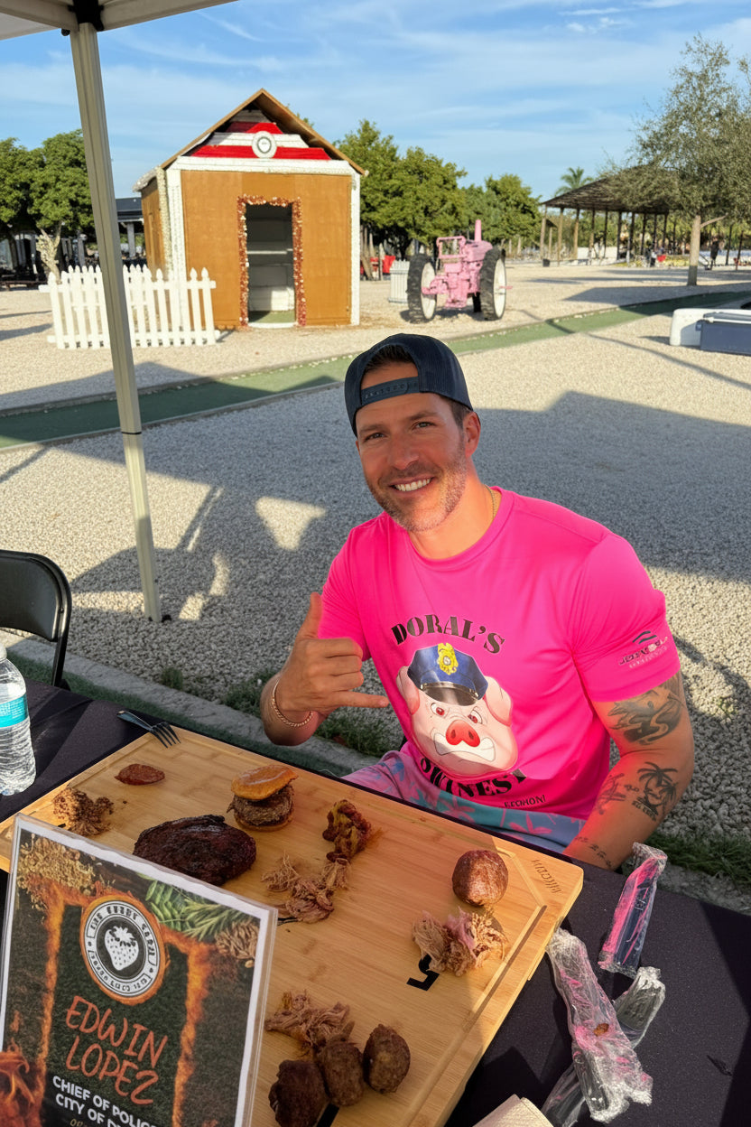 Edwin Lopez in a bright pink graphic t-shirt and black cap sits at an outdoor table, eating from a wooden board with various chocolate treats. Another man is seated to his left at The Berry Farm.
